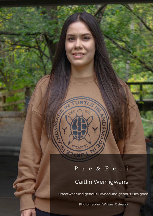 Caitlin Wemigwans, founder of Pre&Peri wearing a brown sweater with a black print of a stylized turtle with the words "Made in Turtle Island" around it.