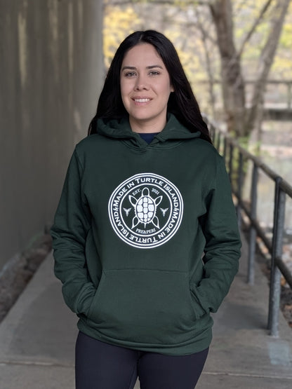 A woman wearing a forest green hoodie with kangaroo pocket. White artwork of a stylized turtle with the words "Made in Turtle Island" around it.